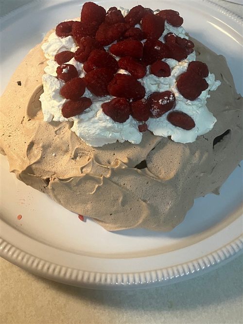 A chocolate pavlova topped with whipped cream and fresh raspberries